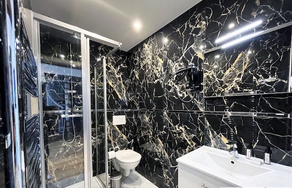 Un baño moderno con cabina de ducha de vidrio, un lavabo blanco y un inodoro.