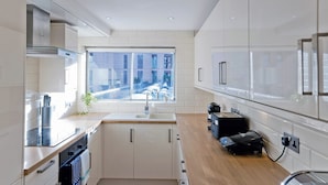 A modern kitchen with white cabinetry, a stainless steel range hood, a window with a city view, and a countertop with a coffee machine. - Imperial Queensway Apartment (London)