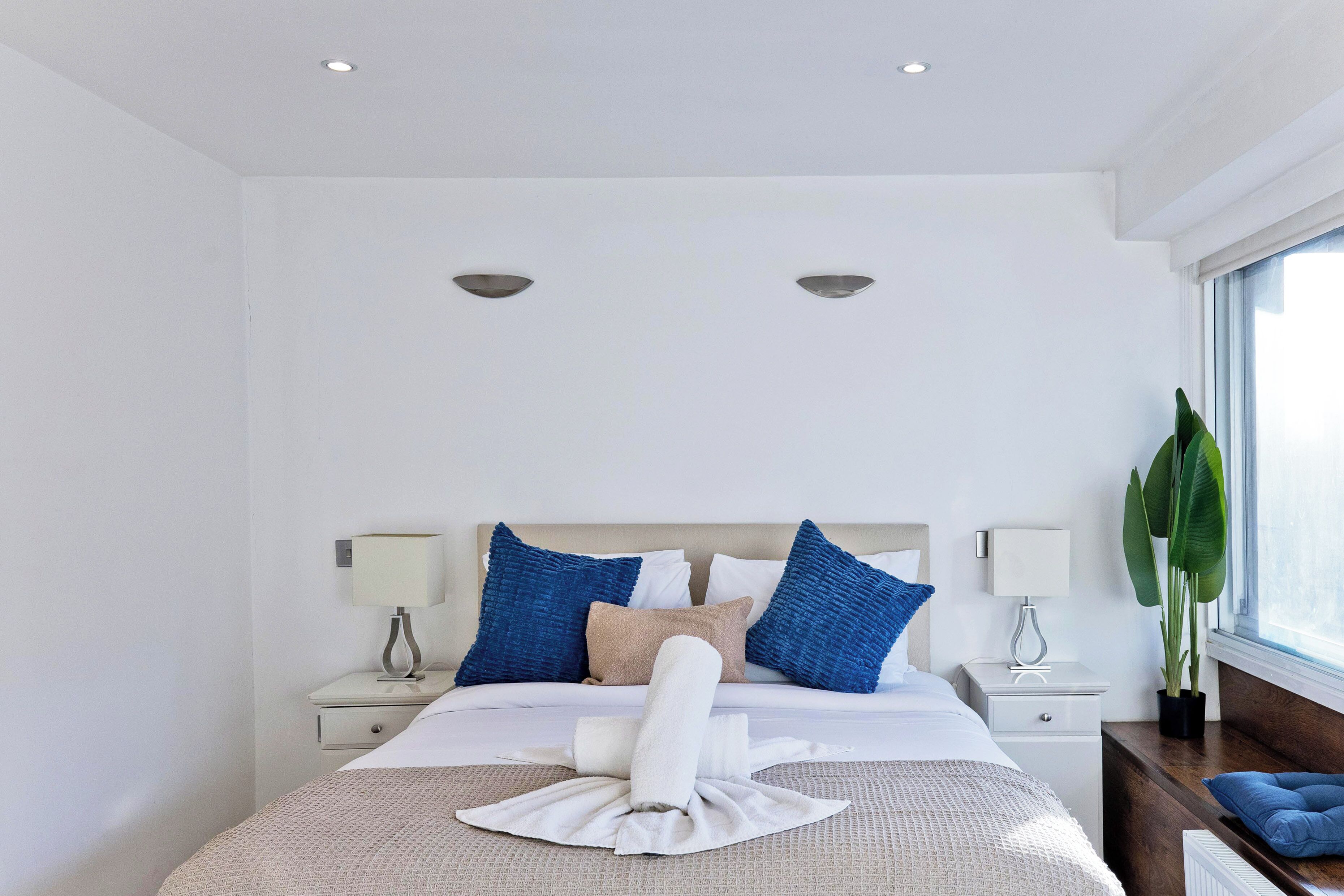 A hotel room with a neatly made bed, two bedside tables with lamps, a large window with a view, and a potted plant.