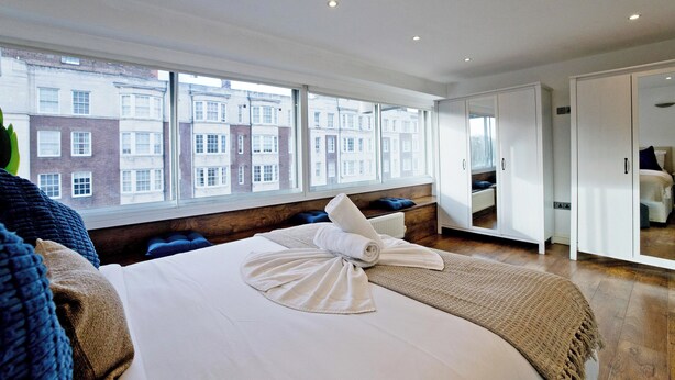 A hotel room with a large window, a bed with a towel, and a wardrobe. - Imperial Queensway Apartment (London)