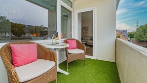 Ein Balkon mit zwei Korbstühlen, einem kleinen runden Tisch und einer Weinflasche.