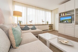Moderni olohuone, jossa on sohva, sohvapöytä, televisio ja kirjahylly.