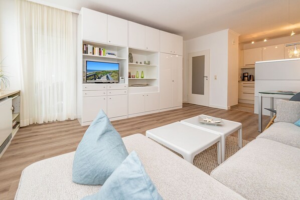 A modern living room with a flat-screen TV, white sofas, and a small dining area.