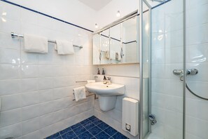 A modern bathroom with white tiles, a glass shower enclosure, a sink with a mirror above it, and a blue-tiled floor. - Lieblingsplatz - Comfortable vacation apartment Lieblingsplatz with balcony and (Sylt)