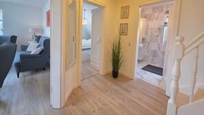 Een hal met een trap, een woonkamer met een bank en een lamp, en een slaapkamer met een bed en een nachtkastje.