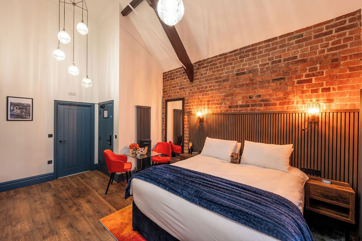Una habitación de hotel moderna con pared de ladrillo, una cama grande, un escritorio con una silla y una butaca roja.