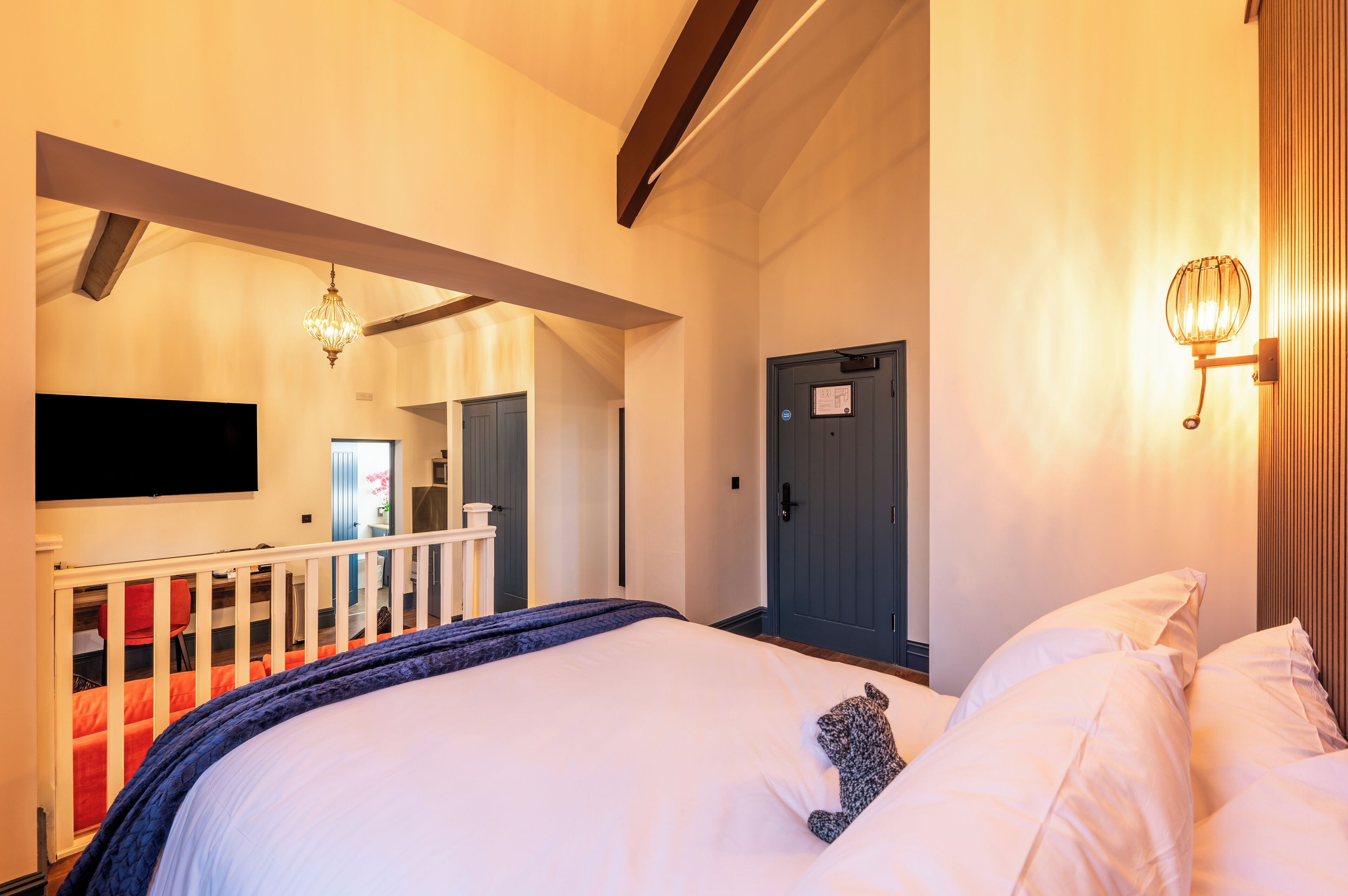 A hotel room with a large bed, a TV mounted on the wall, a balcony with a railing, and a door with a sign.