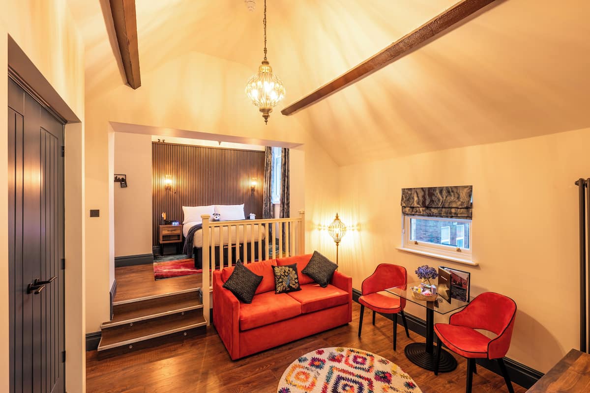 Un salón acogedor con un sofá rojo, una mesa de centro de vidrio y sillas rojas. Se ve una escalera que lleva a otra habitación, un candelabro y una ventana con vistas.