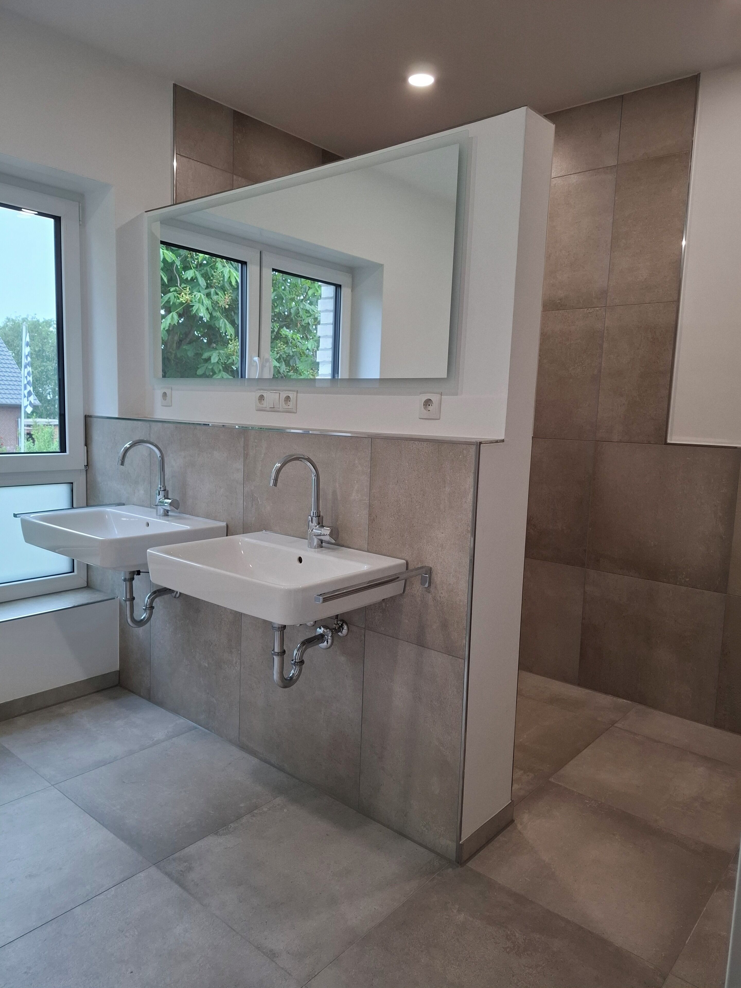 A modern bathroom with two sinks, a large mirror, and a window.