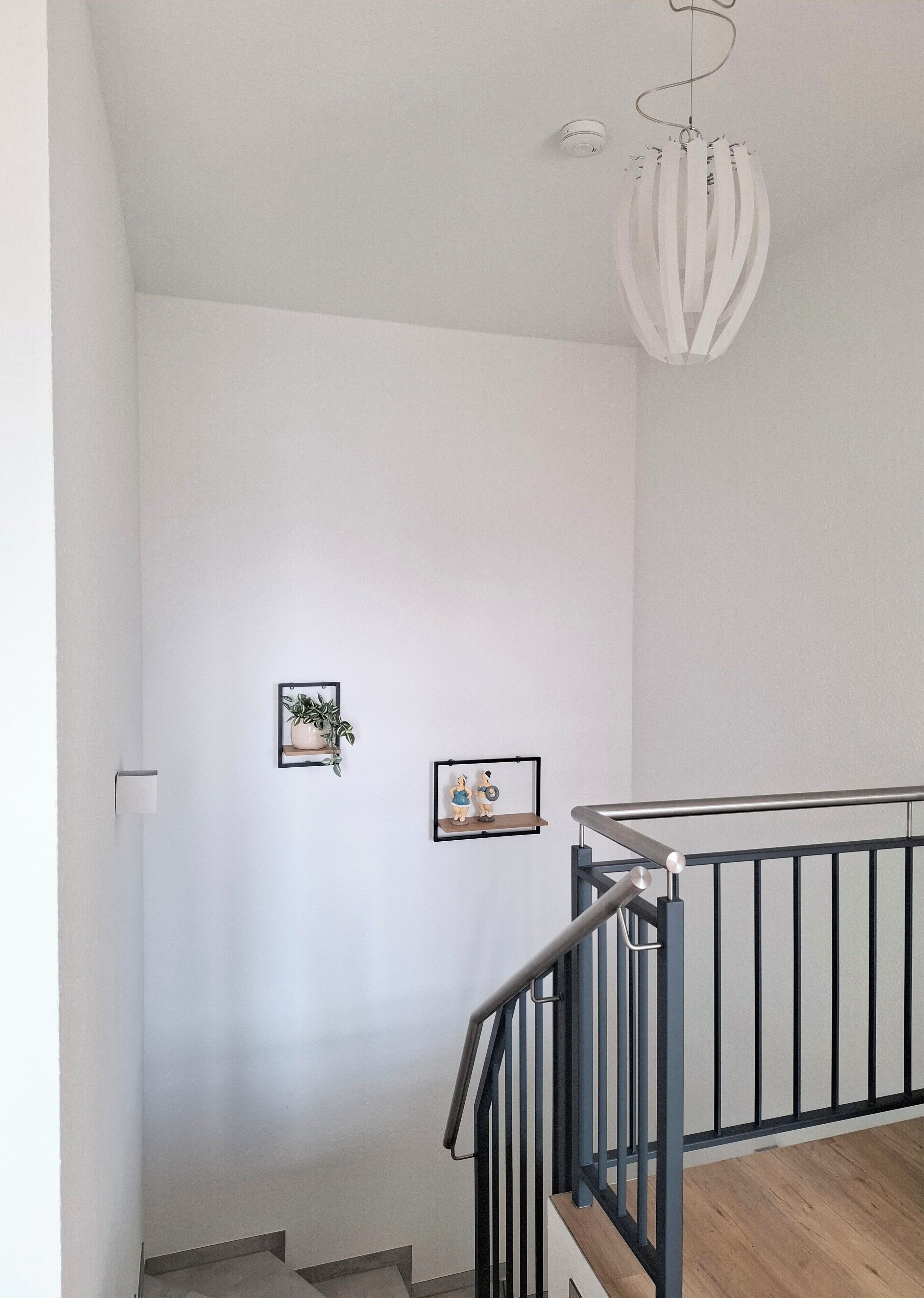 Un escalier avec une rampe en métal, un mur blanc et un luminaire suspendu.