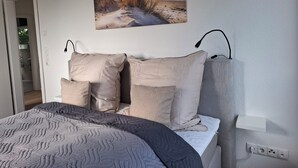 A bedroom with a bed, a nightstand, a lamp, and a painting of a beach scene. - The beach house, up to 8 people, with garden, 200 meters to the lake (Lembruch)