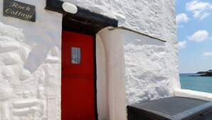 Ein weißes Gebäude mit roter Tür und einem Schild mit der Aufschrift 'Rock Cottage'.