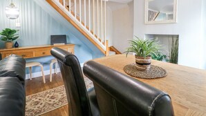 A dining area with a wooden table, black leather chairs, a wooden bench, and a staircase with white railings. - Corner Cottage (Ashbourne)