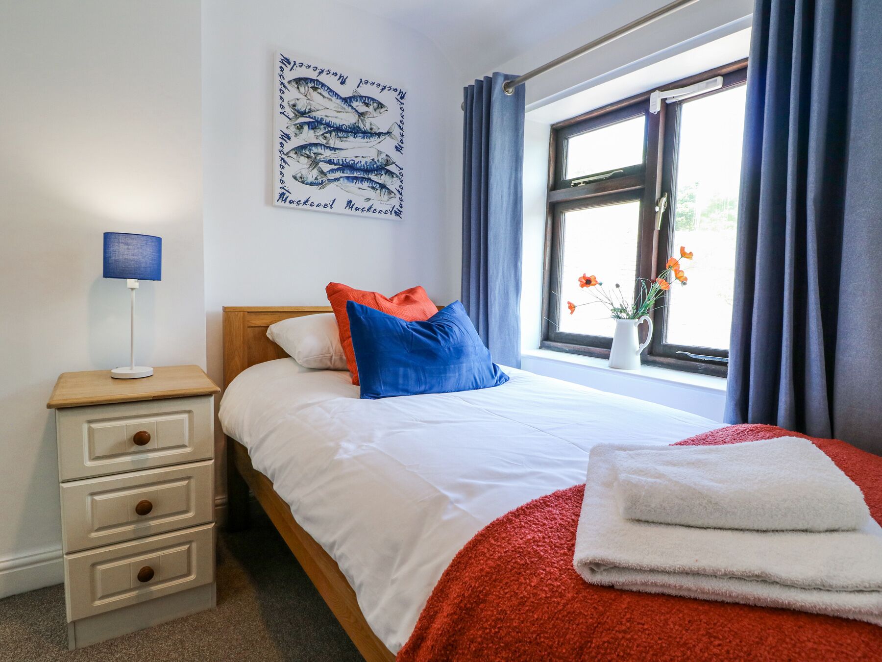 A bedroom with a bed, a nightstand, a lamp, a window with curtains, and a wall art piece.