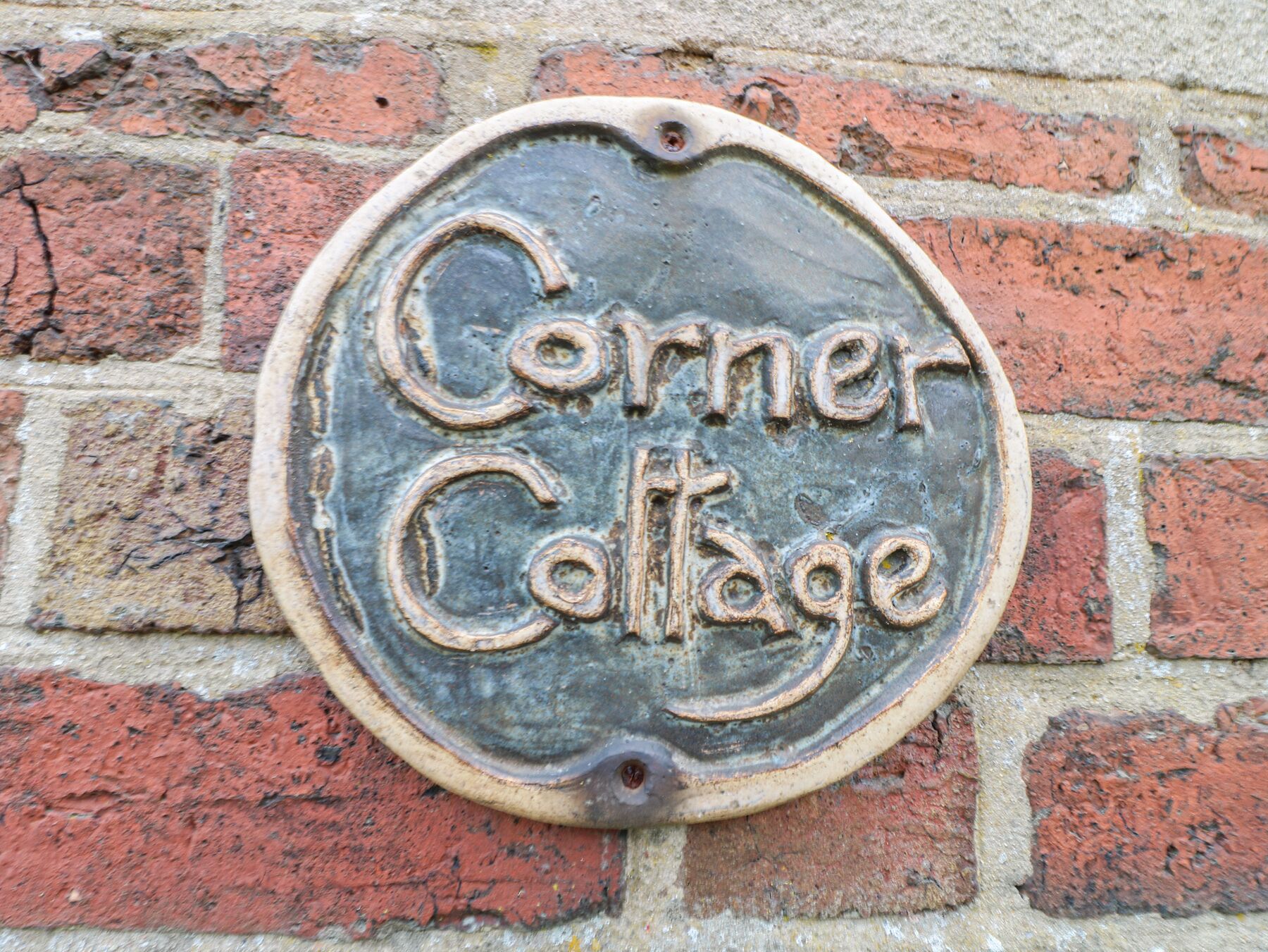 Una placa metálica con la inscripción 'Corner Cottage' colocada en una pared de ladrillo.