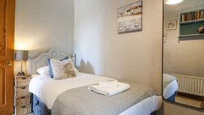 A neatly made bed with a white duvet, a grey throw, and a folded white towel. A painting of boats is on the wall, and a mirror reflects part of the room. - Corner Cottage (Ashbourne)