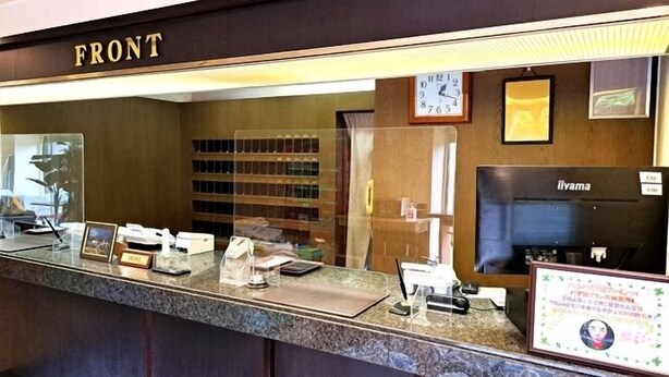 A reception desk with a 'FRONT' sign, a clock, a coffee machine, and a framed certificate on the wall.