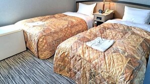 A hotel room with two beds, a nightstand with a lamp, and a small table.