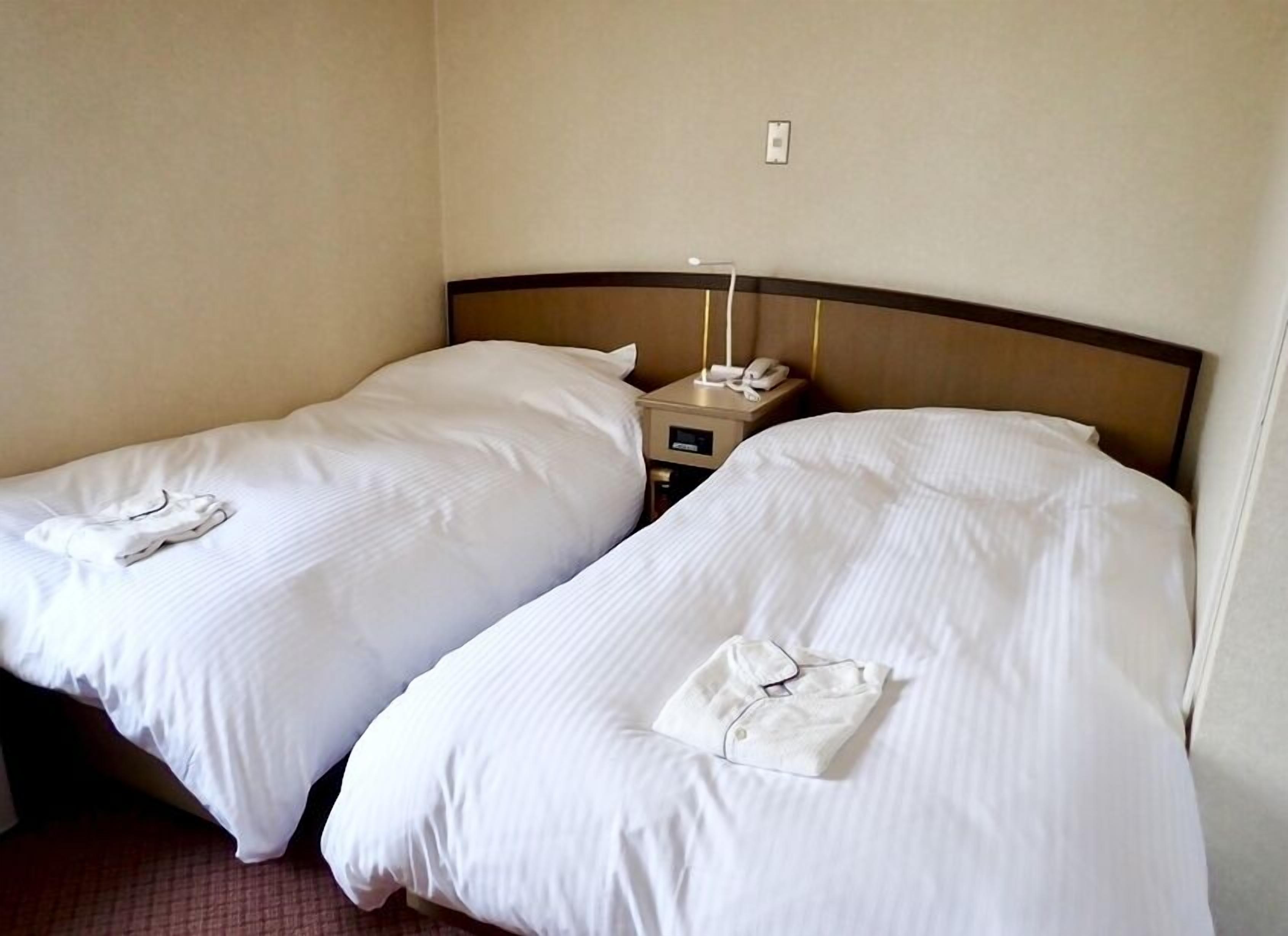Two single beds with white linens, a bedside table with a phone, and a wall socket.