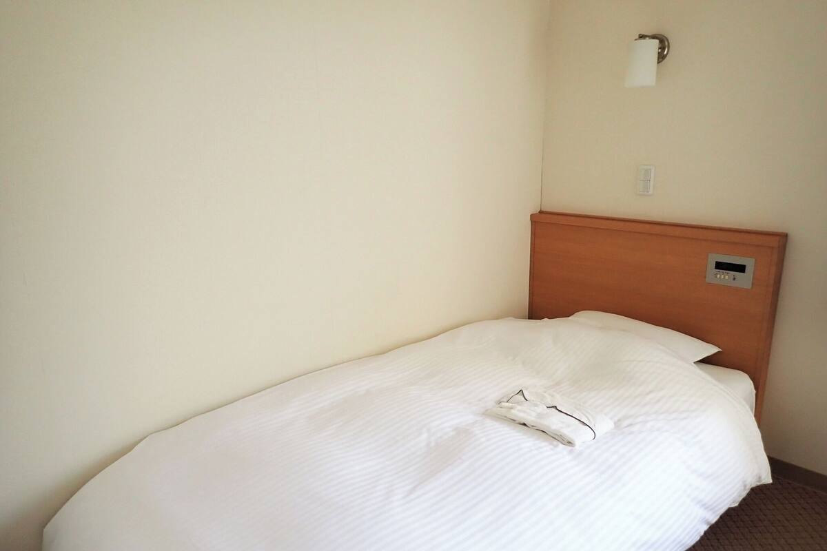 Una cama individual con cabecera de madera, una lámpara de pared y un panel de control en la cabecera.