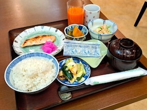 Un plateau contenant du riz, des légumes, un morceau de poisson, un verre de jus d’orange et une théière.