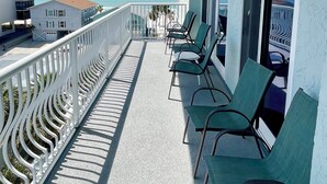 Ein Balkon mit grünen Stühlen, einem weißen Geländer und Blick aufs Meer.