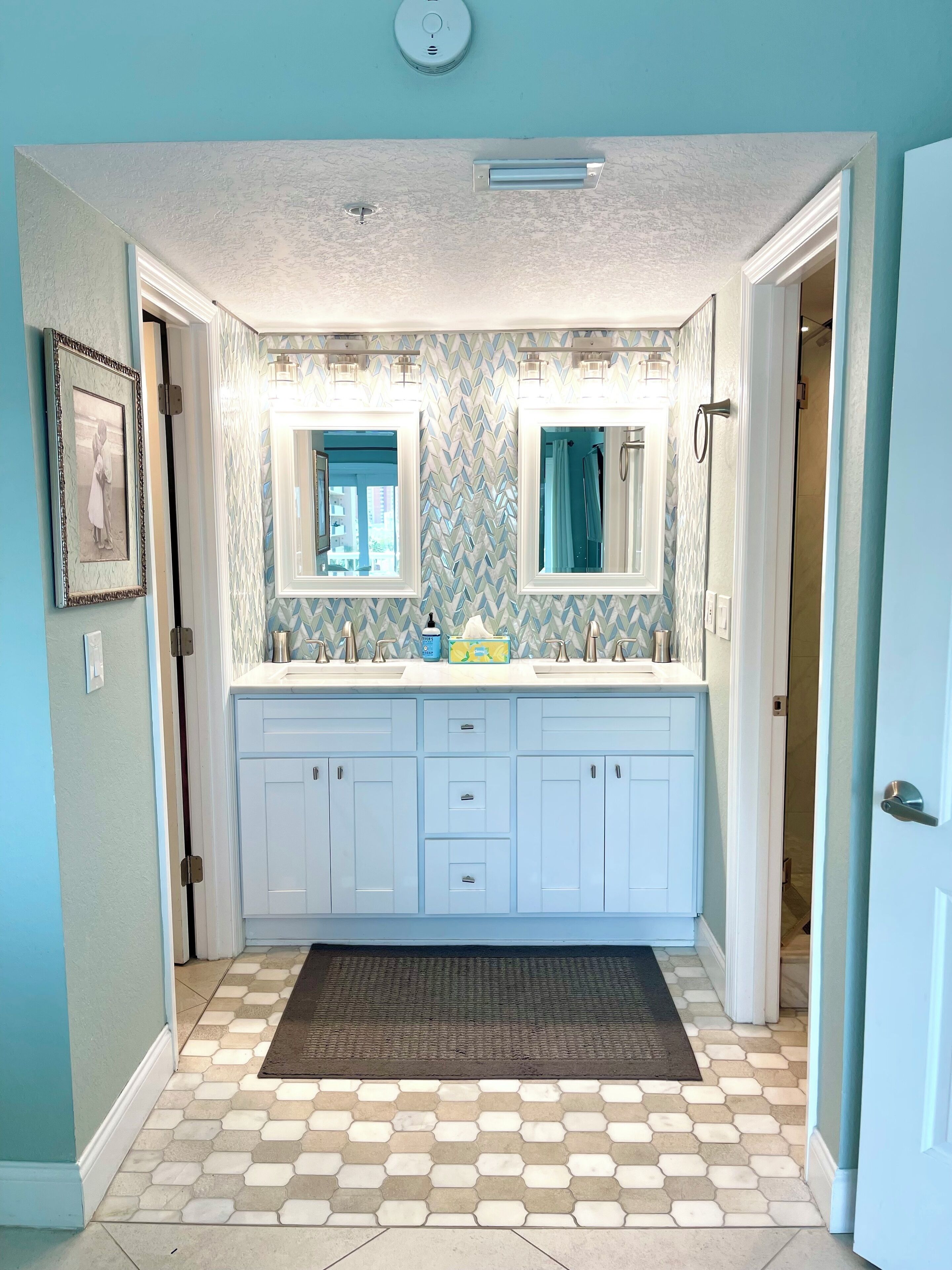 A bathroom with a double sink, white cabinets, a patterned backsplash, and a hexagonal tile floor.