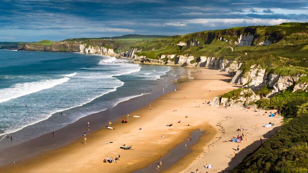 Une plage côtière avec des falaises, un rivage sablonneux et des gens qui profitent de la plage.