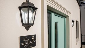 Une entrée d’immeuble avec une porte de couleur turquoise, un luminaire noir fixé au mur et une enseigne indiquant « Dawn Chorus Country ».