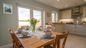 Un coin repas avec une table en bois dressée pour quatre personnes, un vase de tulipes et une vue sur l’extérieur grâce à de grandes fenêtres.