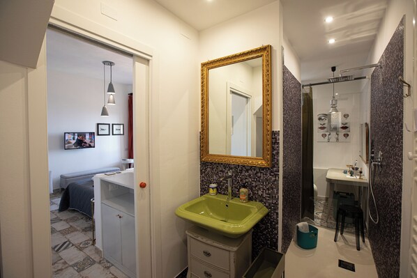 A bathroom with a green sink, a mirror with a gold frame, a shower area, and a small stool.