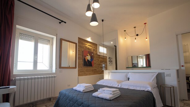 A bedroom with a large bed, a radiator, a window with curtains, a mirror, and a chandelier. - Casuzza at the Dome with a Sea View, within walking distance of the Cathedral! (Agrigento)