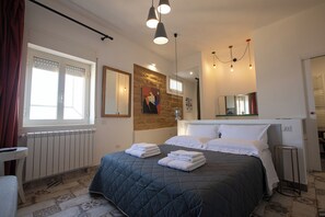 A bedroom with a large bed, a radiator, a window with curtains, a mirror, and a chandelier.