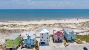 A beachfront property with multiple colorful houses, a sandy beach, and the ocean in the background. - Gulf Front Luxury | Private Heated, Cooled Pool | Elevator and EV Charging (Gulf Shores)