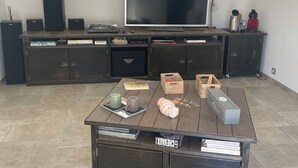 A modern living room with a large flat-screen TV, a wooden coffee table with various items, and a built-in entertainment unit with speakers.