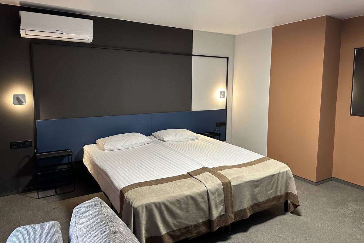 A hotel room with a bed, bedside table, and a wall-mounted air conditioner.
