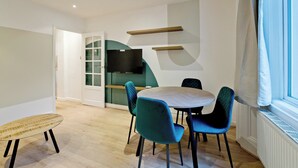A modern dining area with a round table, teal chairs, and a wooden side table. - Imperial Queensborough Terrace (London)