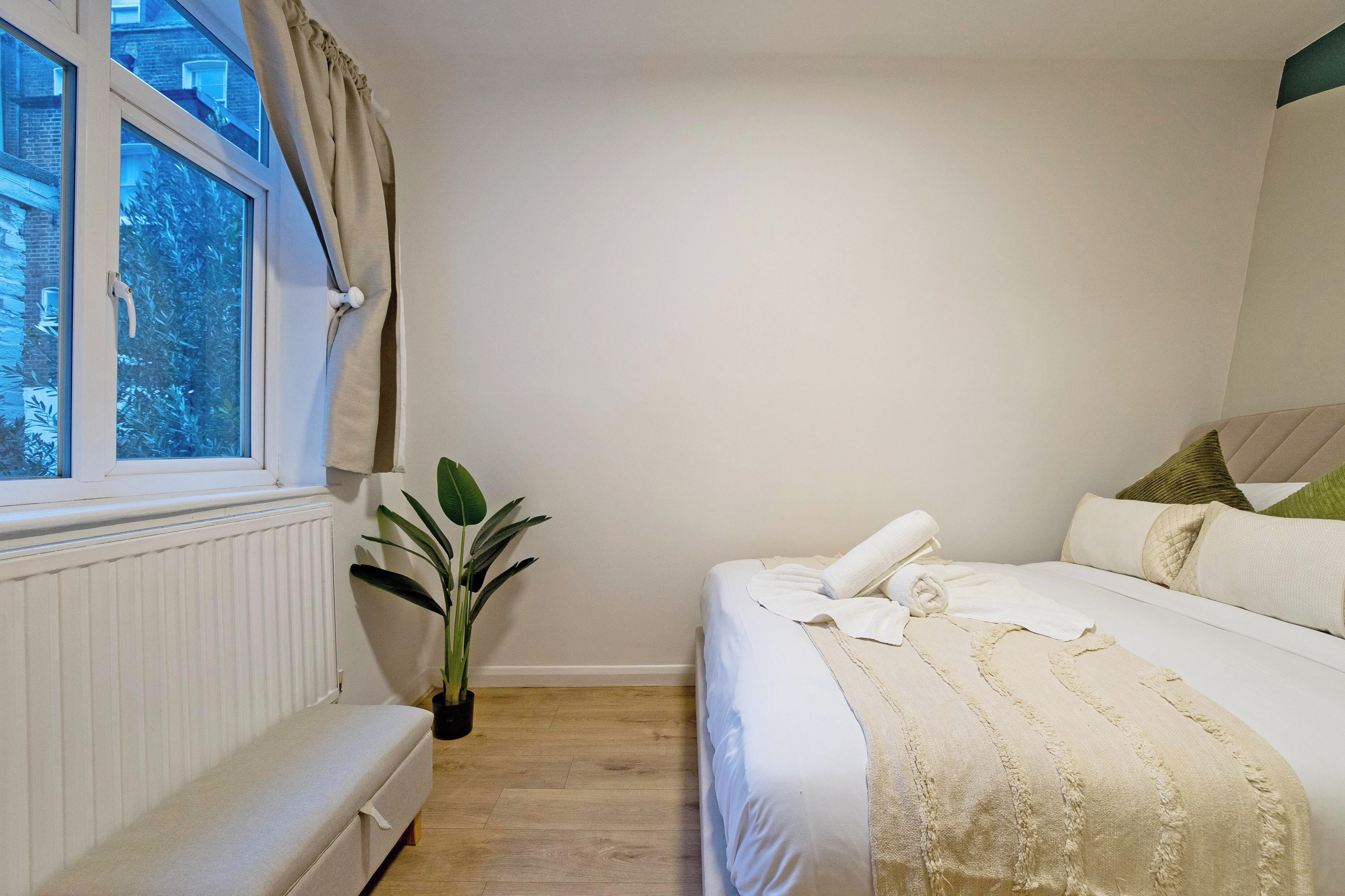 A bedroom with a bed, a bench, a potted plant, and a window with curtains.
