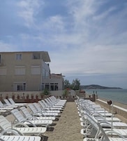 Um hotel à beira-mar com espreguiçadeiras dispostas em fileiras, um edifício com várias janelas e vista para o mar.