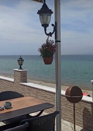 Ein Sitzbereich im Freien mit Tisch und Stühlen, einer hängenden Pflanze und Blick auf das Meer.