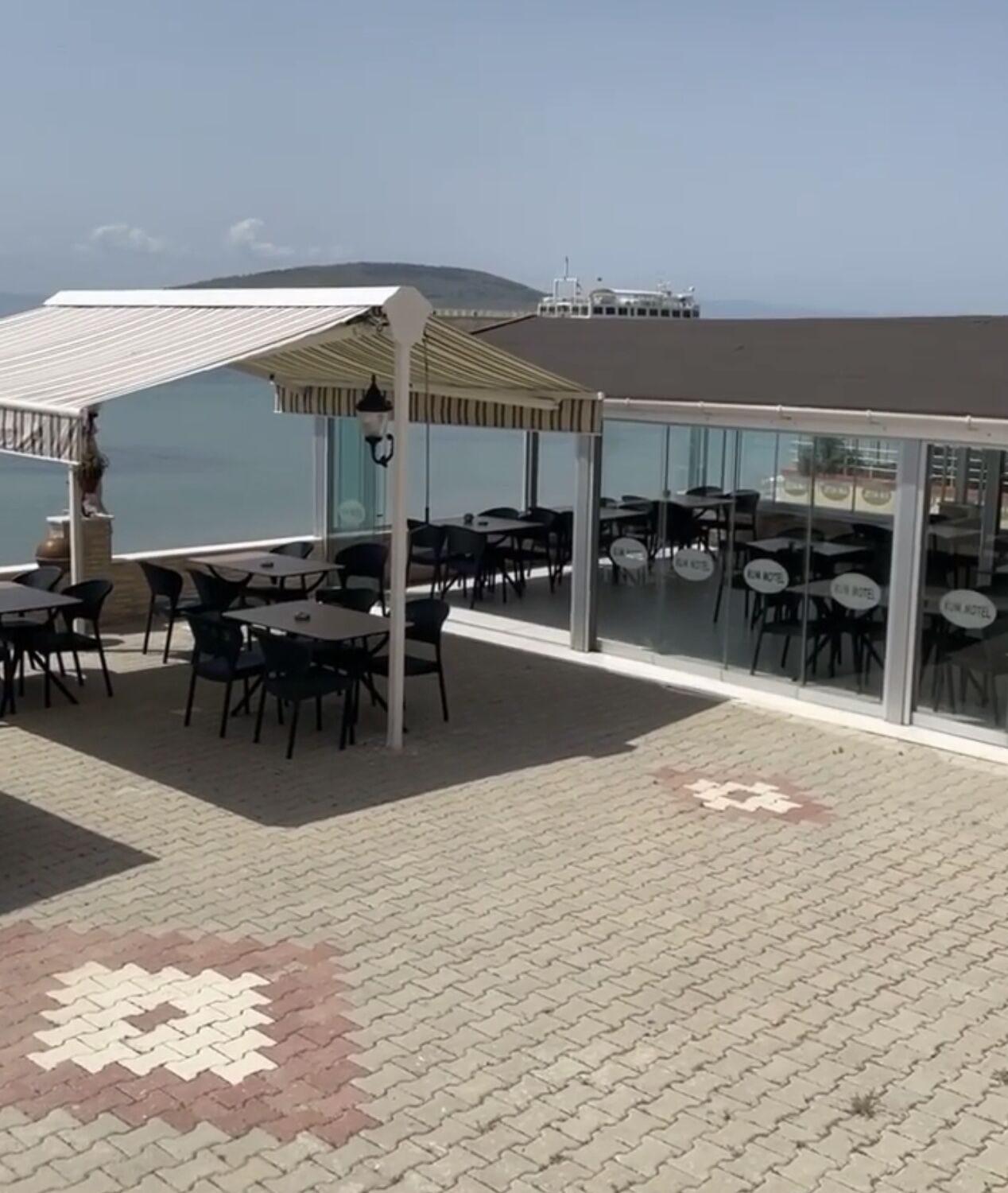 An outdoor seating area with tables and chairs, a covered section, and a view of the sea.