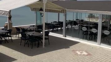 An outdoor seating area with tables and chairs, a covered section, and a view of the sea.