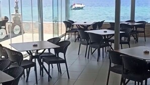 Ein Restaurant mit Tischen und Stühlen, das einen Blick auf ein Gewässer bietet, in dessen Ferne ein Boot zu sehen ist.