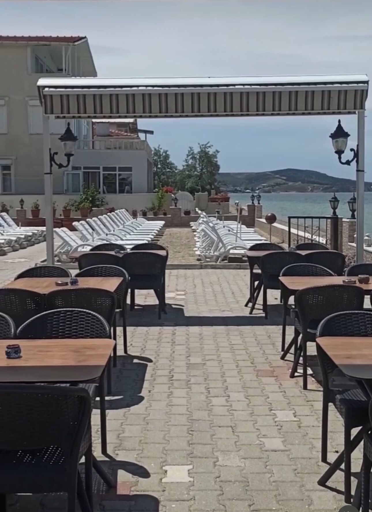 An outdoor seating area with tables and chairs, overlooking a beach and a building in the background.