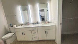 Een badkamer met een wit wastafelmeubel, twee spiegels, een wastafel en een toilet.