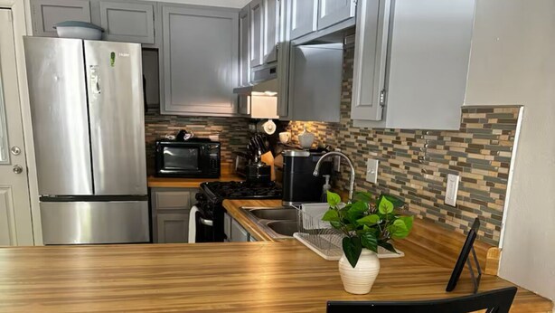 Une cuisine moderne dotée d’appareils électroménagers en acier inoxydable, d’un plan de travail en bois et de deux chaises noires.