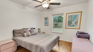 Une chambre à coucher avec un lit, un ventilateur de plafond, une fenêtre et une petite table.