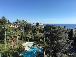 A pool surrounded by palm trees, a clear blue sky, and a view of the ocean and a cruise ship in the distance. - Beautiful ocean view in a quiet luxury residence with a pool and a building manager (Cannes)