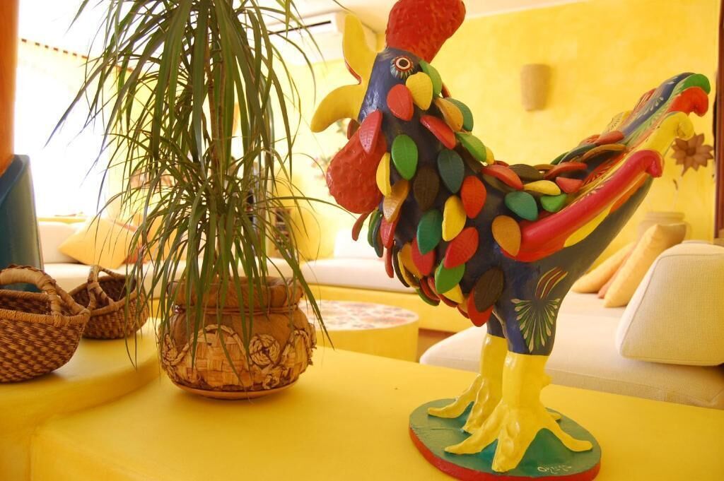 A colorful rooster statue on a yellow table with woven baskets and a potted plant.