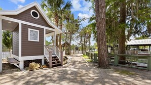A small cabin-style structure with a porch, surrounded by trees and a gravel path. - Winslow Hatch House - Steinhatchee Landing Resort (Steinhatchee)